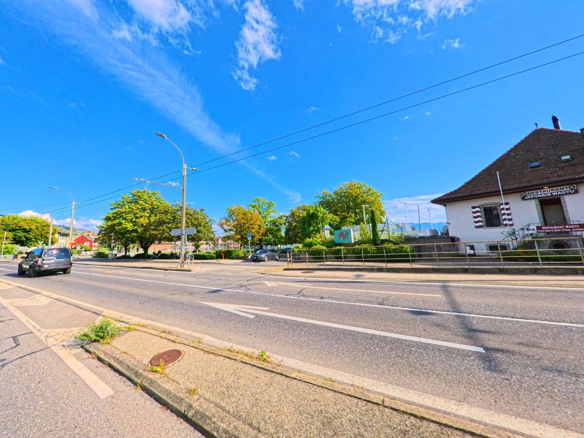 An einer Strasse in Paudex (1094, Kanton Waadt) steht ein Gebaeude mit Restaurantaufschrift, waehrend im Hintergrund Baeume und Masten von Segelbooten sichtbar sind.