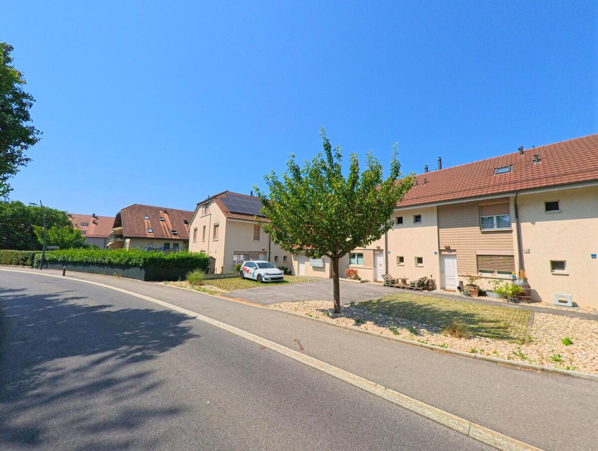 Eine Reihenhaussiedlung mit hellen Fassaden und roten Daechern liegt in Penthaz (1303, Kanton Waadt) an einer ruhigen Seitenstrasse.