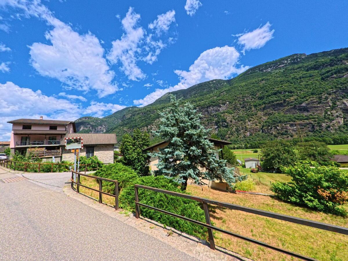 In Personico (6744, Kanton Tessin) verläuft eine ruhige Strasse mit Wohnhäusern und Gärten am Hang unterhalb bewaldeter Berghänge.