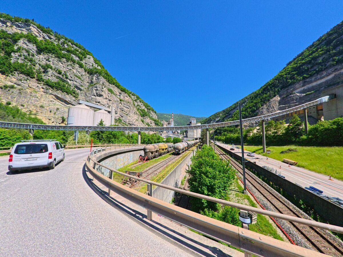 In Péry-La Heutte (2603, Kanton Bern) verläuft eine Straße entlang einer Bahnlinie und Industrieanlage durch ein enges Tal mit steilen Felswänden.