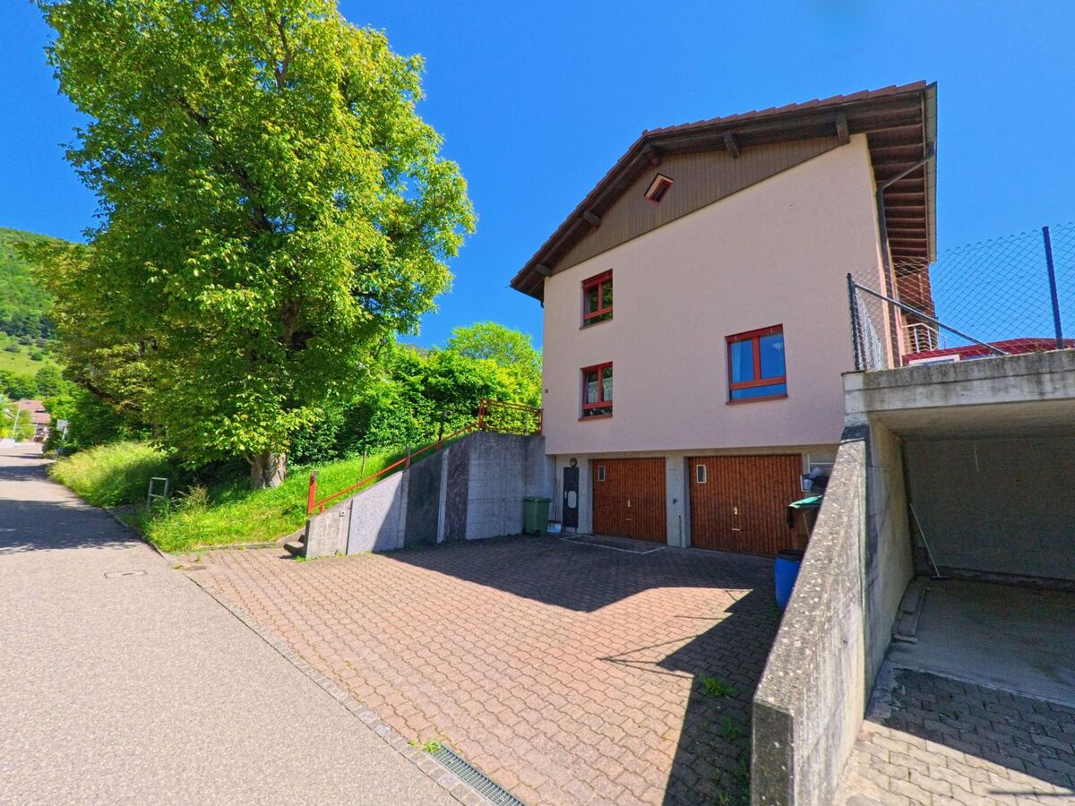 In Péry-La Heutte (2603, Kanton Bern) steht ein Wohnhaus mit Holzgaragen an einem Hang, umgeben von Grünflächen und einem großen Laubbaum.