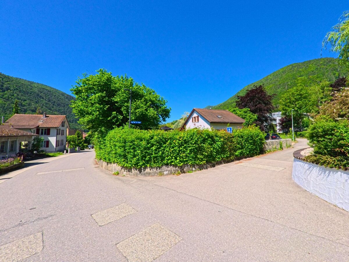 In Péry-La Heutte (2603, Kanton Bern) gabelt sich eine Wohnstraße zwischen gepflegten Hecken und Einfamilienhäusern am Fuße bewaldeter Hügel.