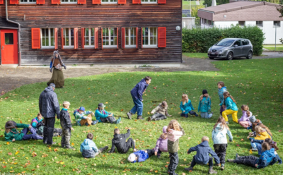 Die Kinder der Pfadi Alpha Centauri verbringen gemeinsam Zeit auf einer grünen Wiese vor einem Holzgebäude in Berikon (8964, Kanton Aargau).