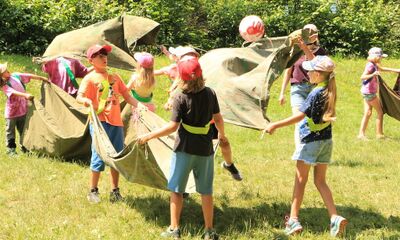 In Brugg (5200, Kanton Aargau) spielen Kinder der Pfadi Brugg im Freien ein Gruppenspiel mit grossen Stoffbahnen auf einer sonnigen Wiese.