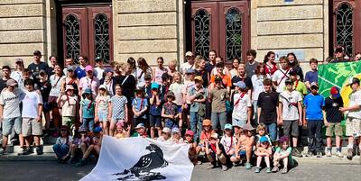 Grosses Gruppenfoto der Pfadi Falkenstein Basel-Binningen mit Kindern, Jugendlichen und Leitenden vor einem historischen Gebäude. Die Teilnehmenden präsentieren Pfadifahnen und stehen für Gemeinschaft, Abenteuer, Verantwortung und aktive Jugendarbeit.