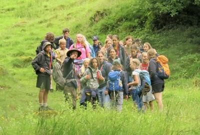 Eine Gruppe von Kindern und Jugendlichen wandert gemeinsam durch eine gruene Landschaft in Waldkirch (9205, Kanton St Gallen) und zeigt Outdoor Aktivitaet.