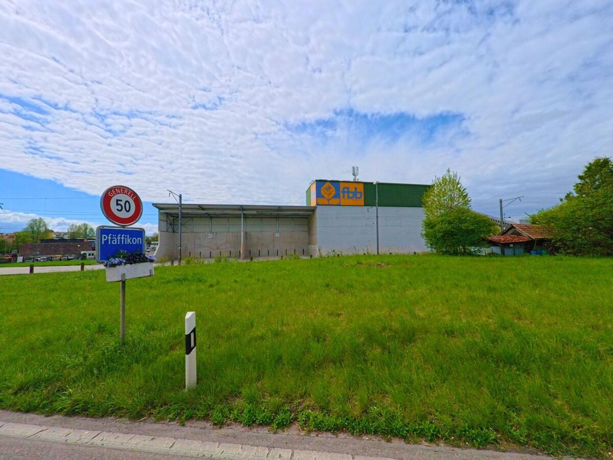 Am Ortseingang von Pfäffikon im Kanton Zürich mit der PLZ 8300 steht ein Verkehrsschild vor einer grossen Industriehalle, eingerahmt von Wiese und Bahnlinie.