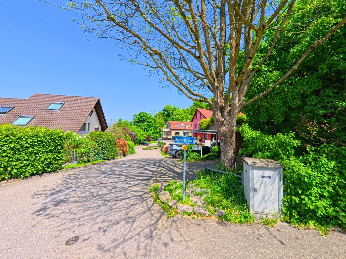 In Pfeffingen (4148, Kanton Baselland) führt eine kleine, von Bäumen gesäumte Strasse an einem Haus entlang. Ein Strassenschild und ein Stromkasten sind ebenfalls sichtbar.