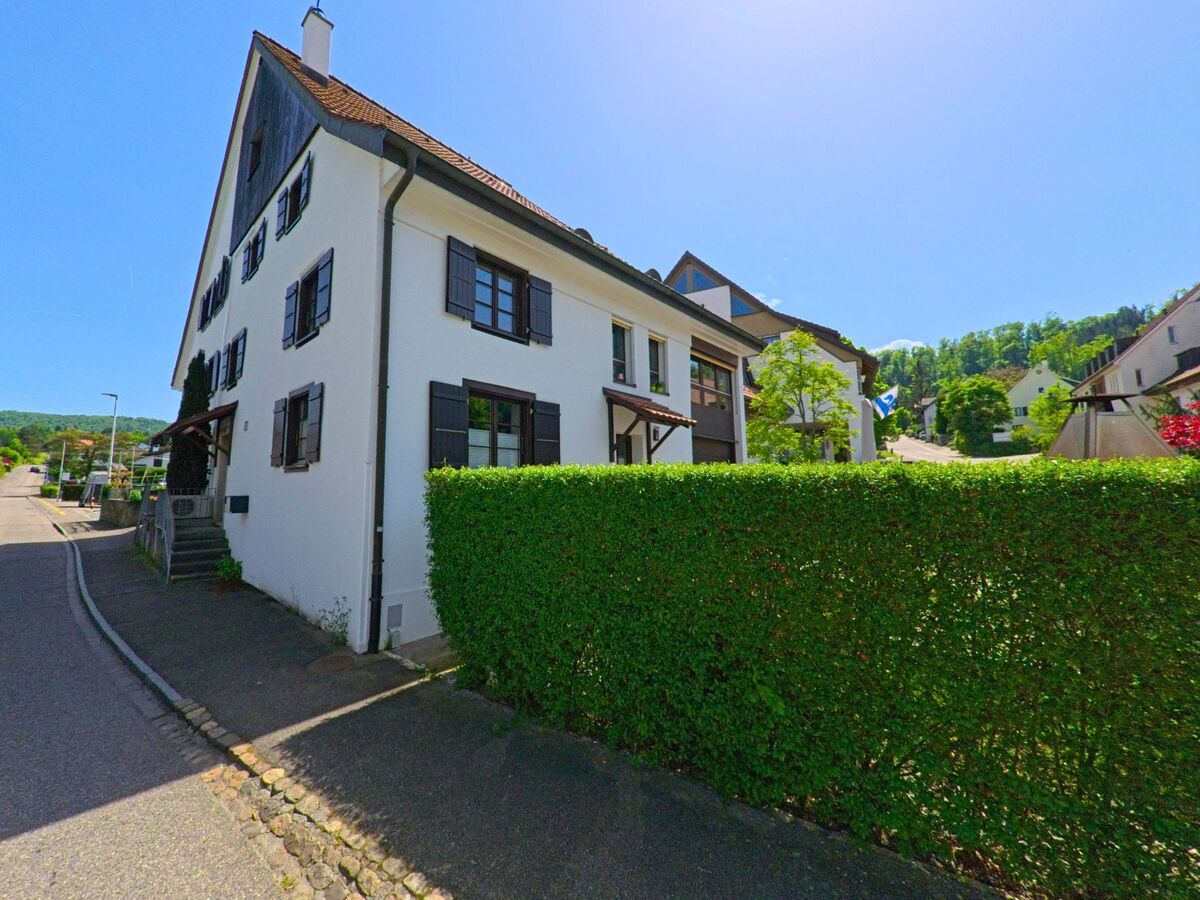 In Pfeffingen (4148, Kanton Baselland) ist ein traditionelles Haus mit einer weissen Fassade und einem gepflegten Garten zu sehen. Eine Strasse verläuft neben dem Gebäude.