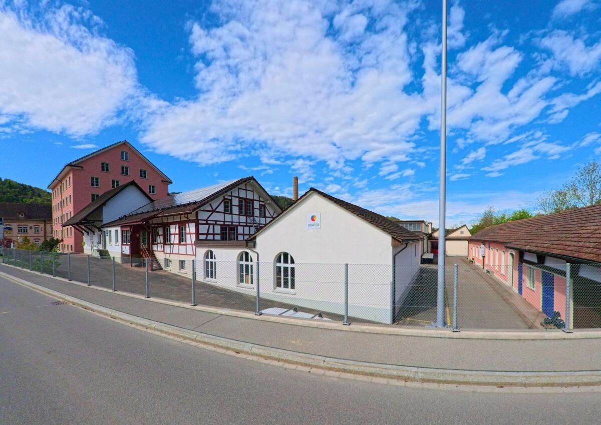 In der Gemeinde Pfungen im Kanton Zürich, PLZ 8422, stehen historische und moderne Gewerbebauten mit Sicht auf ein Fachwerkhaus hinter einem Metallzaun.