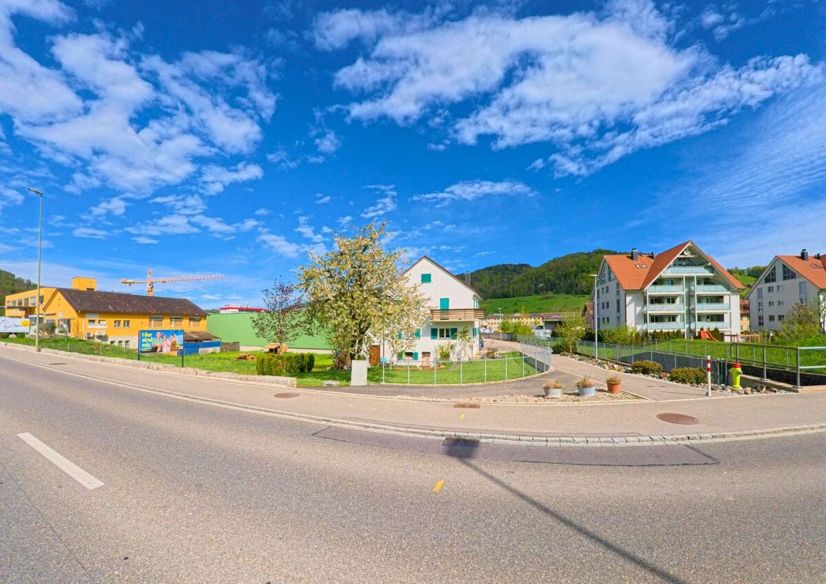 In Pfungen im Kanton Zürich, PLZ 8422, verläuft eine Hauptstrasse an einer gemischten Bebauung mit Einfamilienhaus, Neubauten und Gewerbehallen entlang.