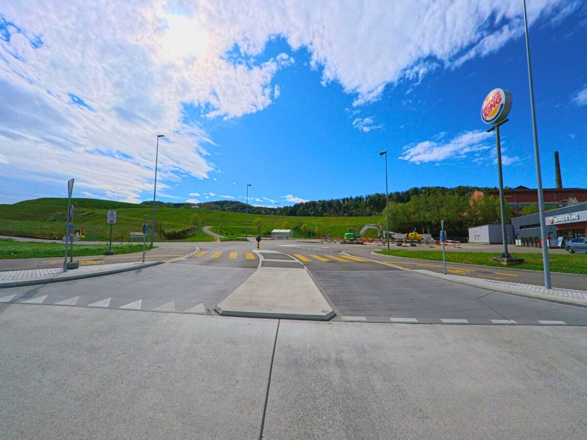  In Pfungen im PLZ-Gebiet 8422 im Kanton Zürich liegt ein Fast-Food-Restaurant an einer Kreuzung mit Blick auf Felder, Hügel und eine Baustelle.