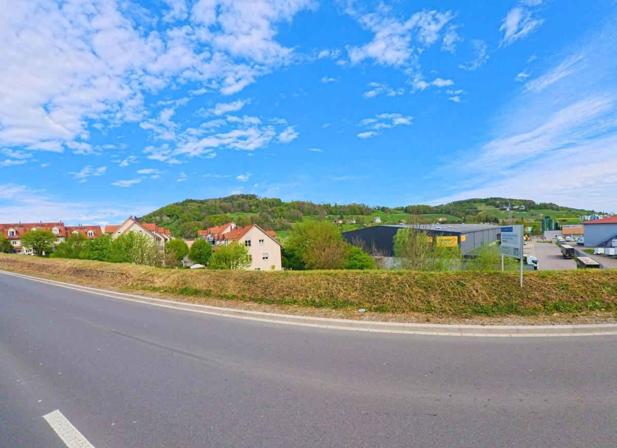 In Pfungen im Kanton Zürich, PLZ 8422, trifft eine Wohnsiedlung mit roten Dächern auf ein angrenzendes Gewerbegebiet am Rande einer Landstrasse.