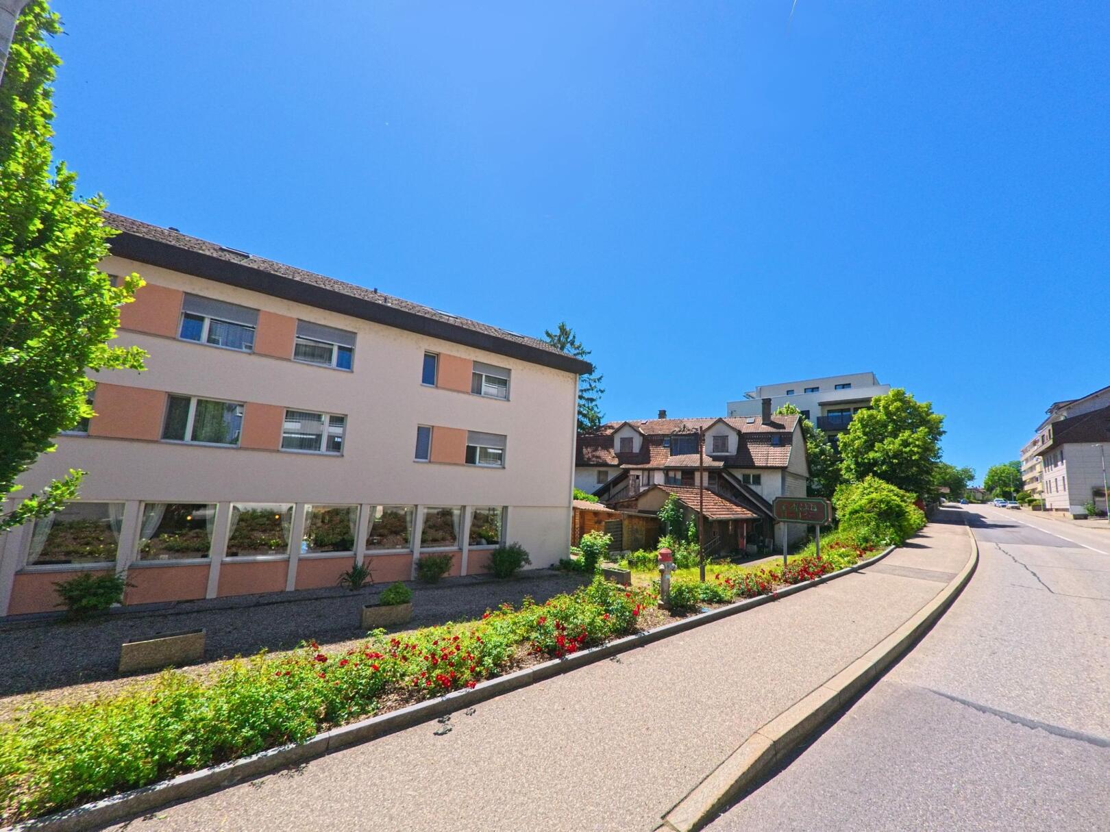 In Pieterlen (2542, Kanton Bern) reihen sich entlang einer leicht ansteigenden Strasse moderne und ältere Gebäude, darunter ein Hotel mit gepflegter Gartenanlage.