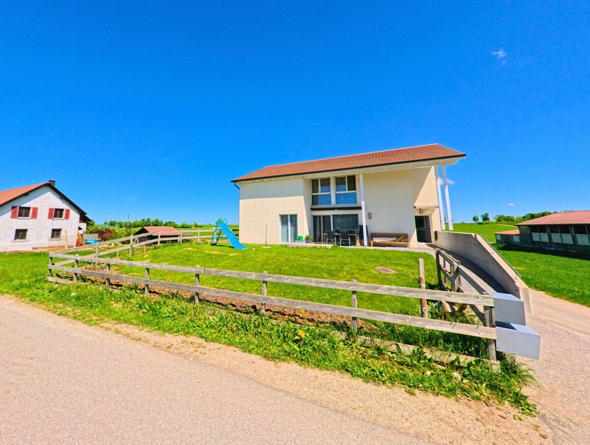 In Pleigne (2807, Kanton Jura) liegt ein modernes Einfamilienhaus mit Spielplatz auf einer kleinen Anhöhe, umgeben von ländlicher Bebauung und offenen Feldern.