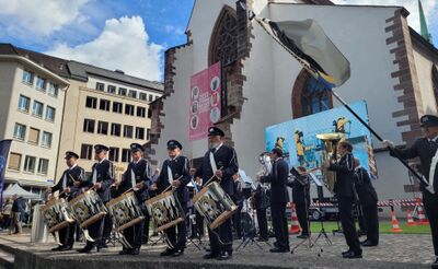 In Basel (4000, Kanton Basel-Stadt) tritt die Polizeimusik Basel in Uniform vor historischer Kulisse auf, waehrend Trommler und Blaeser ein Freiluftkonzert gestalten.
