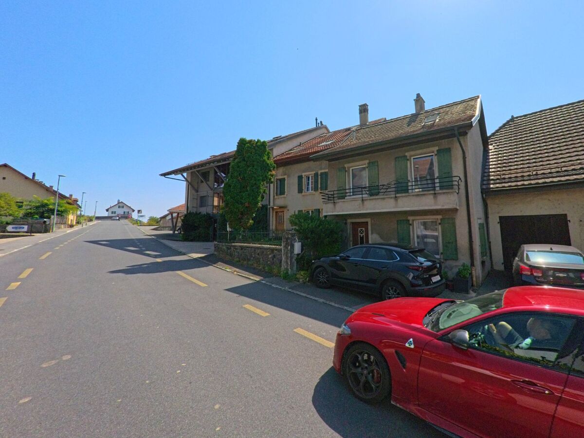 Mehrere Wohnhaeuser mit gruene Fensterlaeden und Balkonen reihen sich entlang einer Strasse in Pompaples (1318, Kanton Waadt).