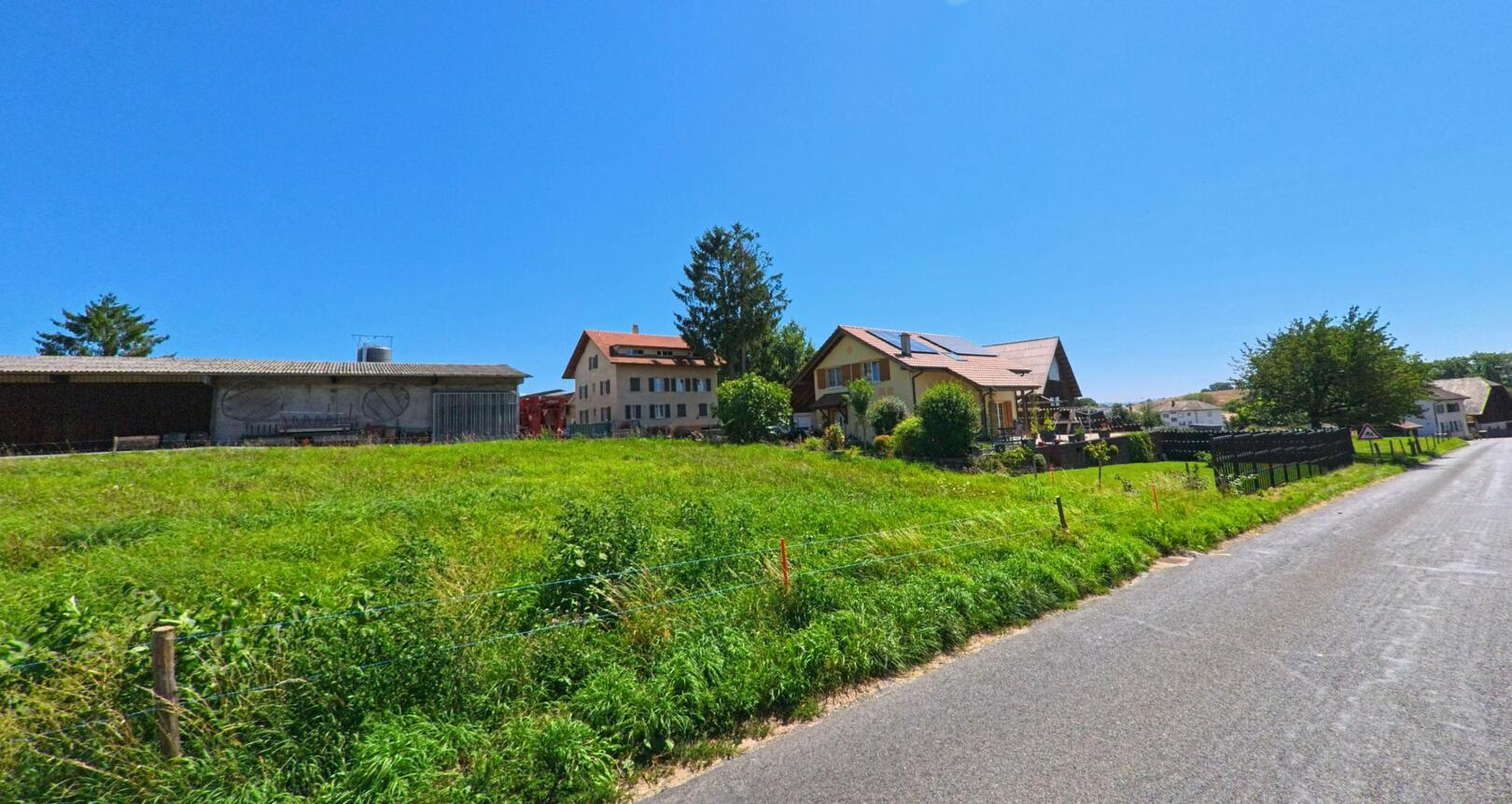 Entlang einer schmalen Landstrasse in Ponthaux (1757, Kanton Freiburg) stehen gepflegte Bauernhäuser mit roten Dächern und grünen Wiesen im Vordergrund.