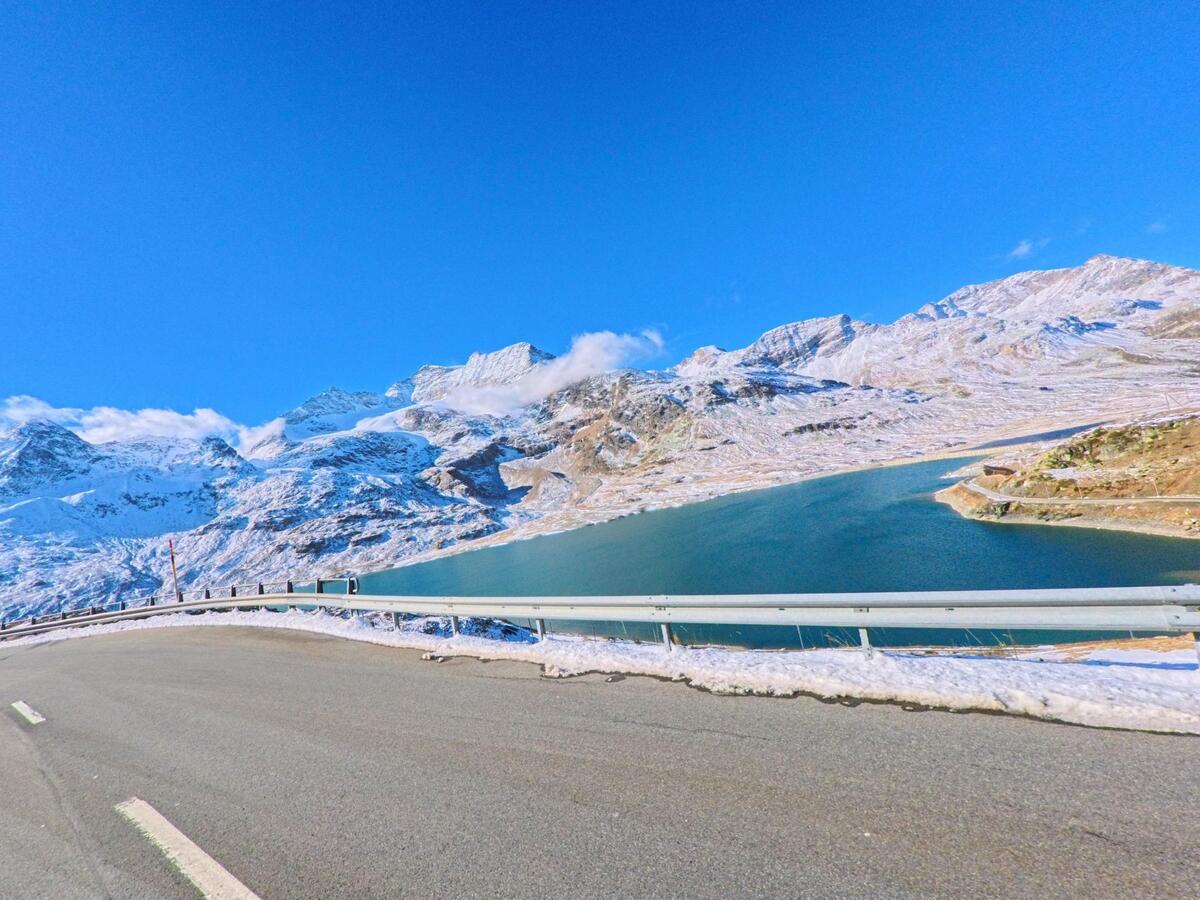 Entlang einer hoch gelegenen Passstrasse bei Pontresina (7504, Kanton Graubünden) öffnet sich der Blick auf einen tiefblauen Bergsee unter schneebedeckten Gipfeln.