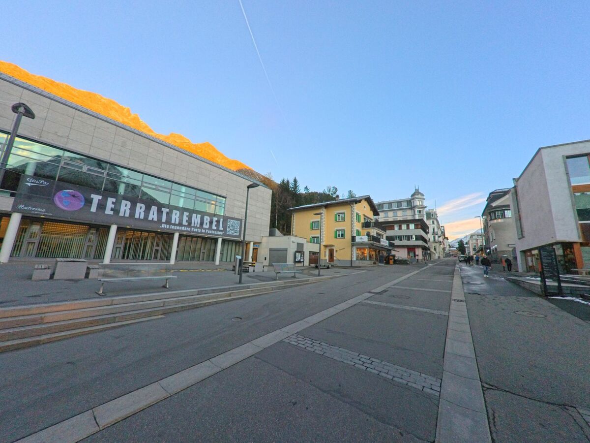An einer zentralen Strasse in Pontresina (7504, Kanton Graubünden) prägen moderne Gebäude und traditionelle Häuser das ruhige Ortsbild im frühen Abendlicht.