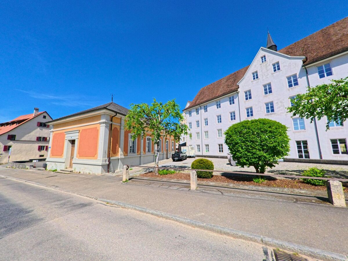 In Porrentruy (2900, Kanton Jura) stehen ein barockes Nebengebäude in warmem Ockerton und ein langgestreckter, weiss verputzter Hauptbau mit steilem Dach auf einem offenen Platz.