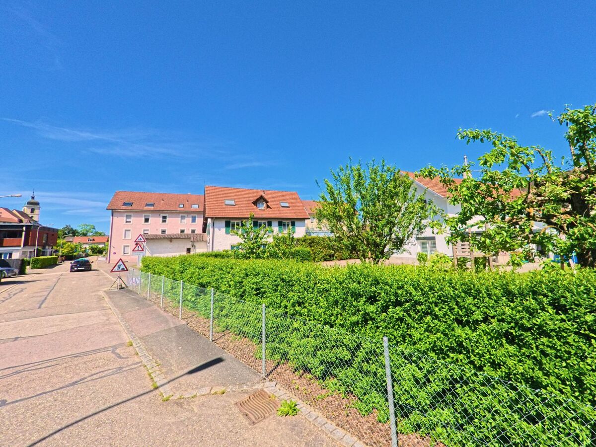 In einem Wohngebiet von Porrentruy (2900, Kanton Jura) säumen Einfamilienhäuser mit roten Dächern eine ruhige Strasse, im Hintergrund ist der Kirchturm sichtbar.