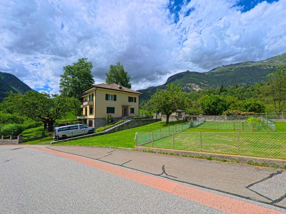 Ein helles Wohnhaus mit Garten und Obstbäumen steht in Prato (Leventina) (6773, Kanton Tessin) auf einer leicht ansteigenden Wiese mit Blick auf bewaldete Berghänge.