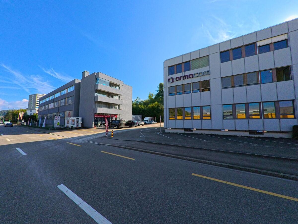 In Pratteln (4133, Kanton Basel-Landschaft) stehen moderne Gewerbegebäude entlang einer vielbefahrenen Strasse, wobei breite Fensterfronten und klare Linien das Gebiet prägen.