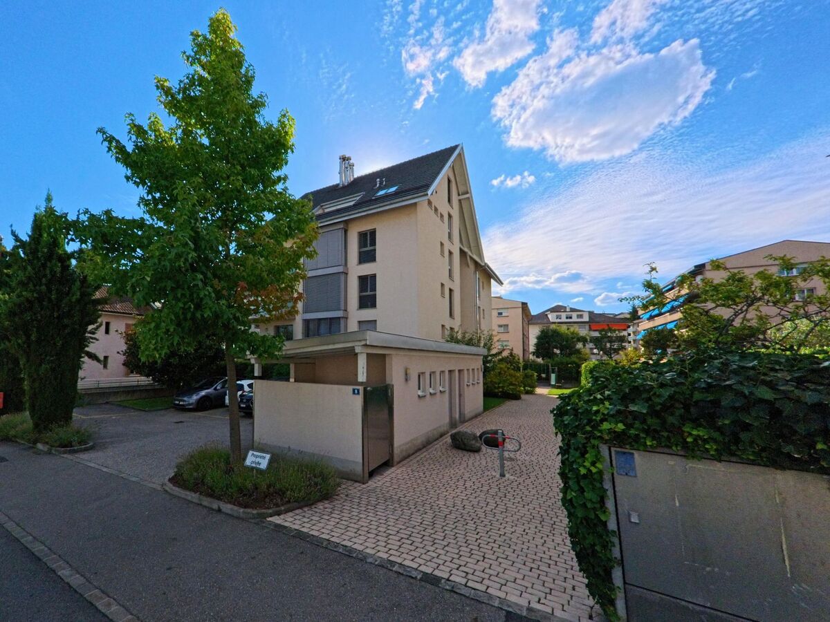 Ein modernes Wohnhaus mit Satteldach und mehreren Balkonen steht inmitten einer ruhigen Wohnsiedlung in Pully (1009, Kanton Waadt), umgeben von Gruenanlagen.