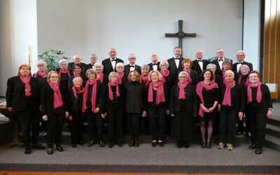 In einem Kirchenraum in Thun (3602, Kanton Bern) steht eine Gruppe von Personen in einheitlicher Kleidung vor einem Kreuz fuer ein gemeinsames Gruppenbild.