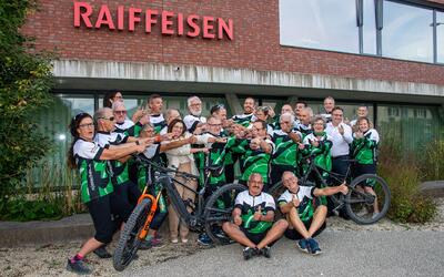 Vor einem Gebäude in Jonschwil (9243, Kanton St.Gallen) posiert der Radclub Jonschwil in grün-schwarzen Trikots mit Fahrrädern für ein Gruppenfoto.