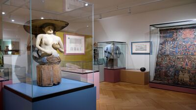 Im Raetischen Museum in Chur (7000, Kanton Graubuenden) sind historische Objekte wie eine bemalte Holzfigur, Textilien und Uniformen in Glasvitrinen ausgestellt.