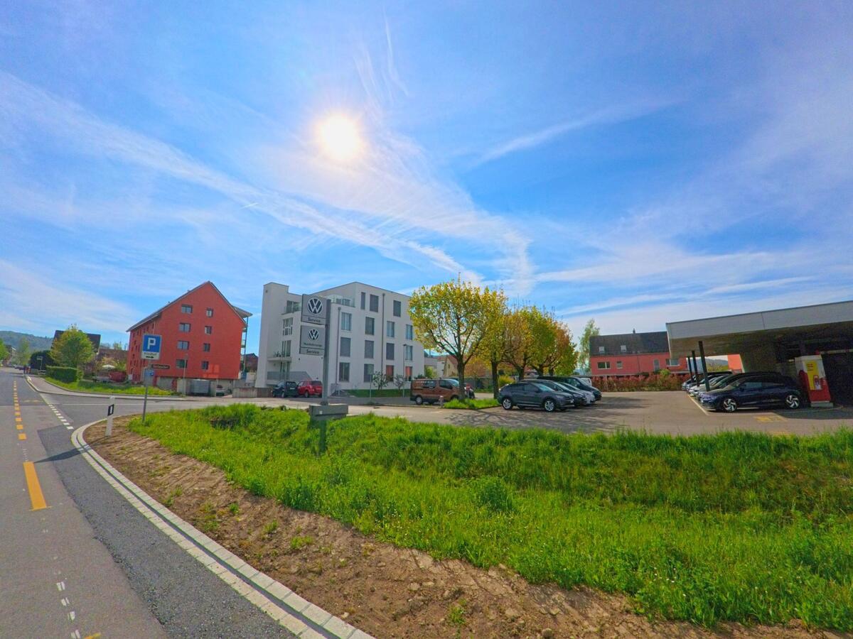 In Rafz im Kanton Zürich, PLZ 8197, befindet sich ein modernes Autohaus mit Parkplatz an einer breiten Strasse, umgeben von Wohnbauten und Bäumen.