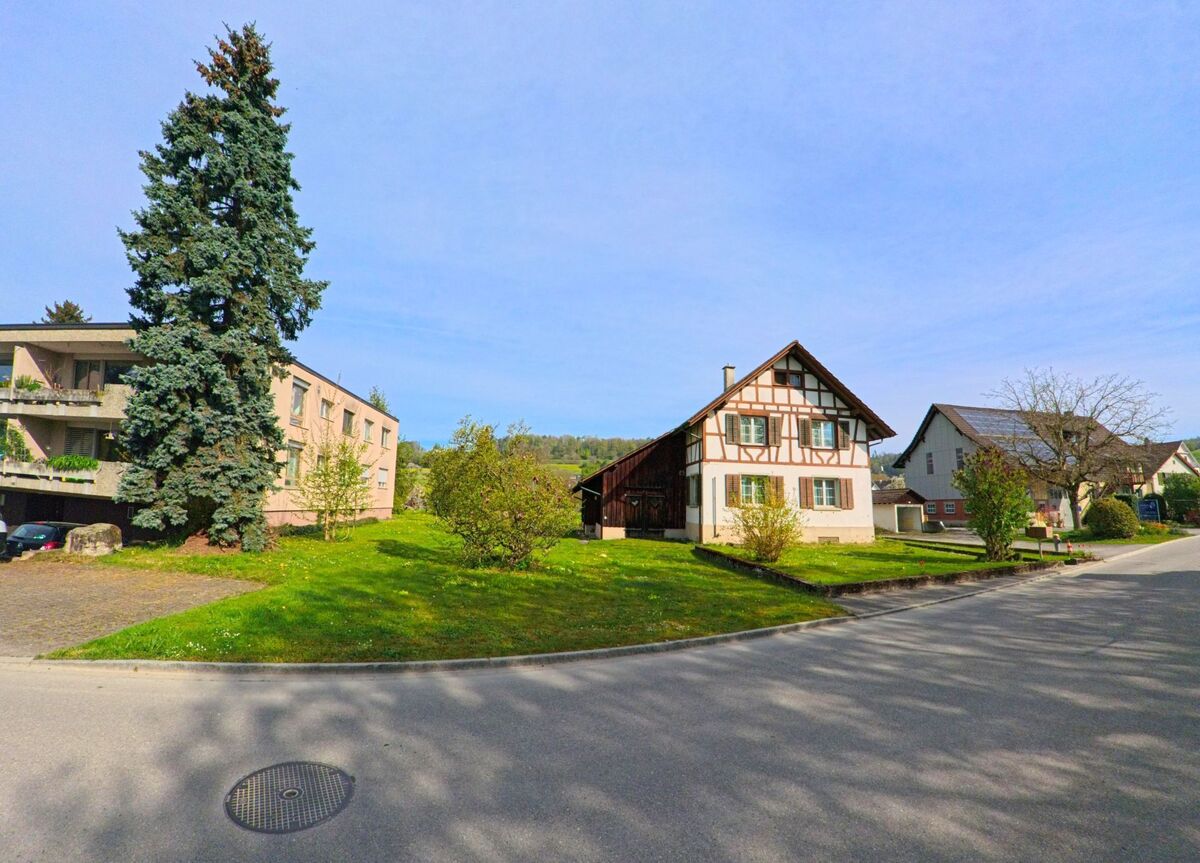 In Rafz im PLZ-Gebiet 8197 im Kanton Zürich stehen ein traditionelles Fachwerkhaus und moderne Wohnbauten inmitten gepflegter Grünflächen.