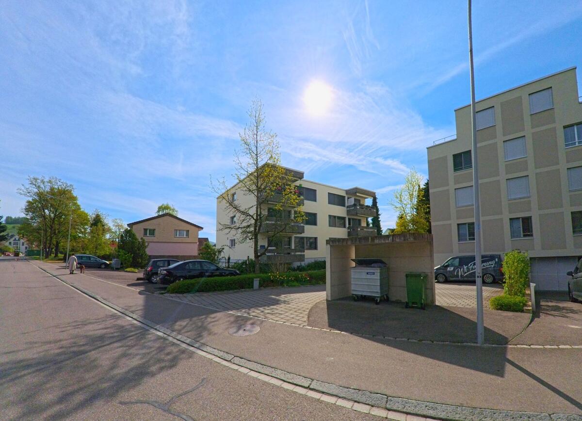 In Rafz im Kanton Zürich mit der PLZ 8197 erstreckt sich eine ruhige Wohnsiedlung mit modernen Mehrfamilienhäusern, Parkplätzen und einem überdachten Abfallplatz.