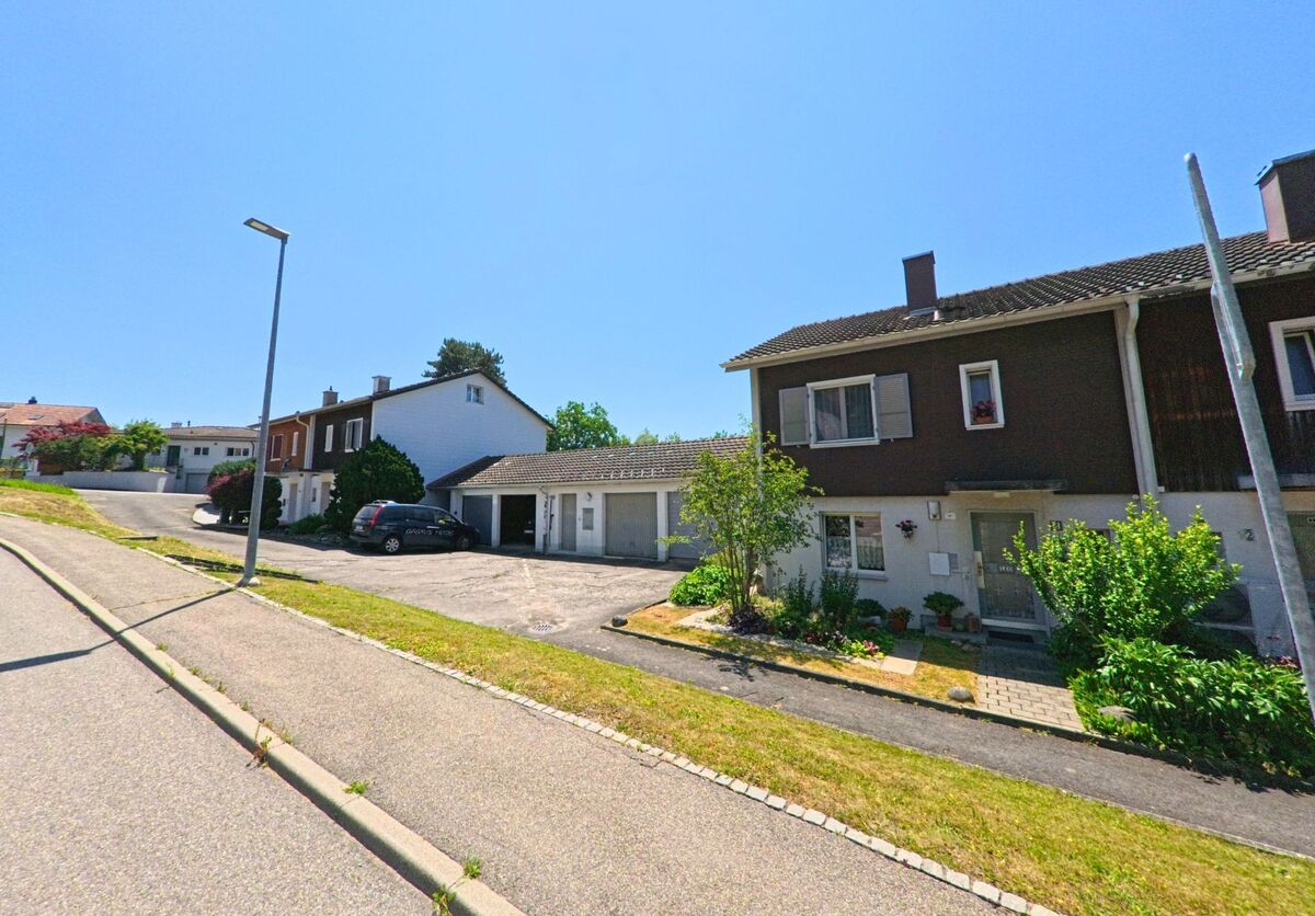 In Rapperswil (3053, Kanton Bern) befinden sich Reihenhäuser entlang einer ruhigen Straße, mit Gärten und parkenden Autos im Vordergrund.