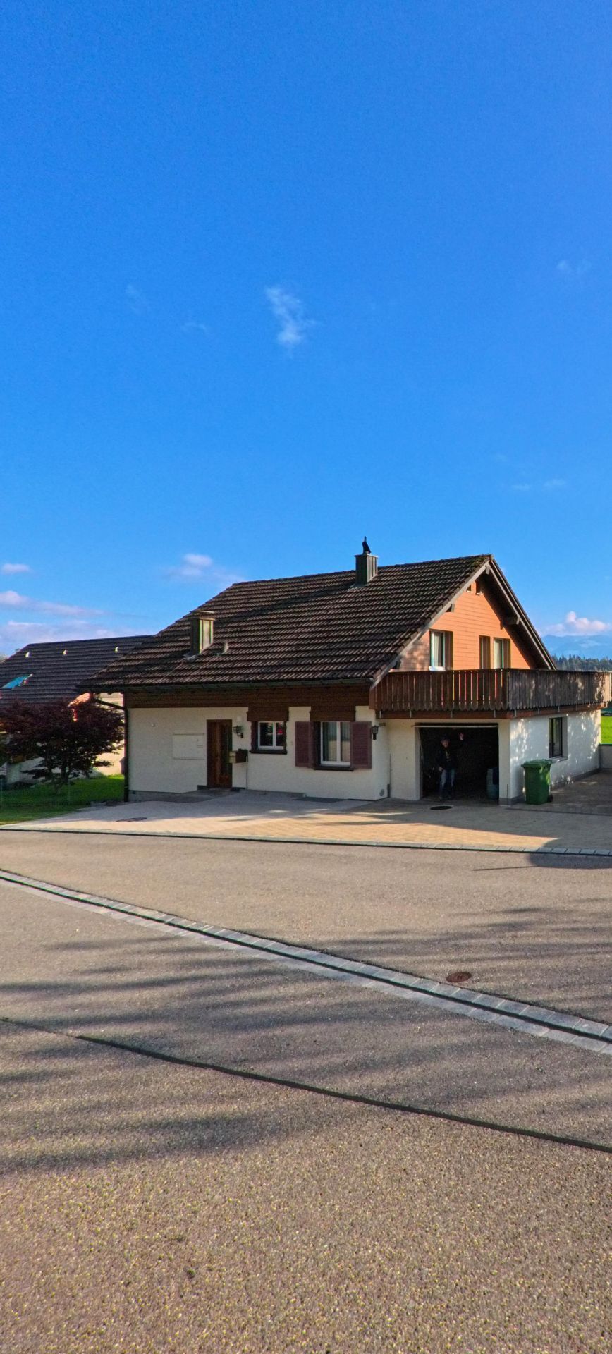 Ein Wohnhaus mit gedecktem Vorplatz und Balkon steht in Rapperswil-Jona (8640, Kanton St. Gallen) an einer ruhigen Strasse vor einem weiten Himmel.