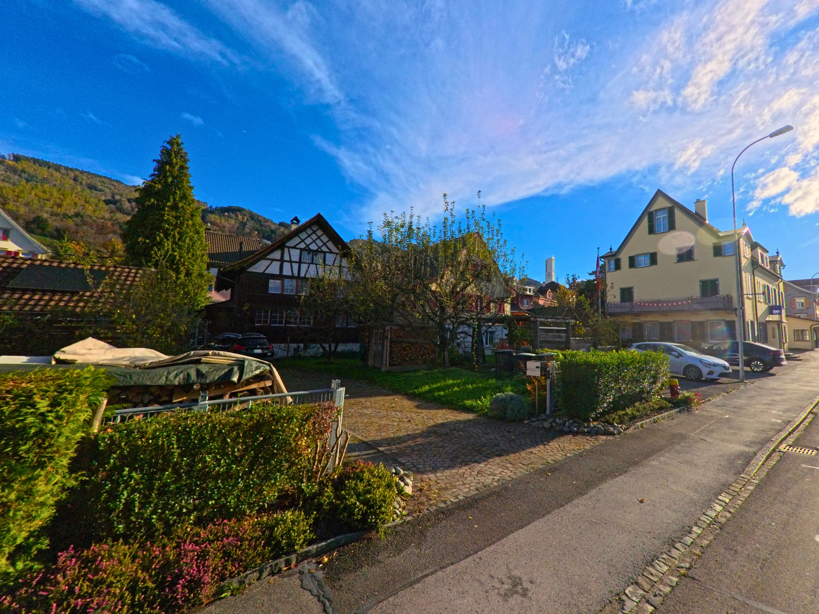 Entlang einer ruhigen Wohnstrasse mit gepflegten Gärten zeigt sich ein historisch geprägtes Quartier in Rebstein 9445 im Kanton St. Gallen bei klarem Himmel.