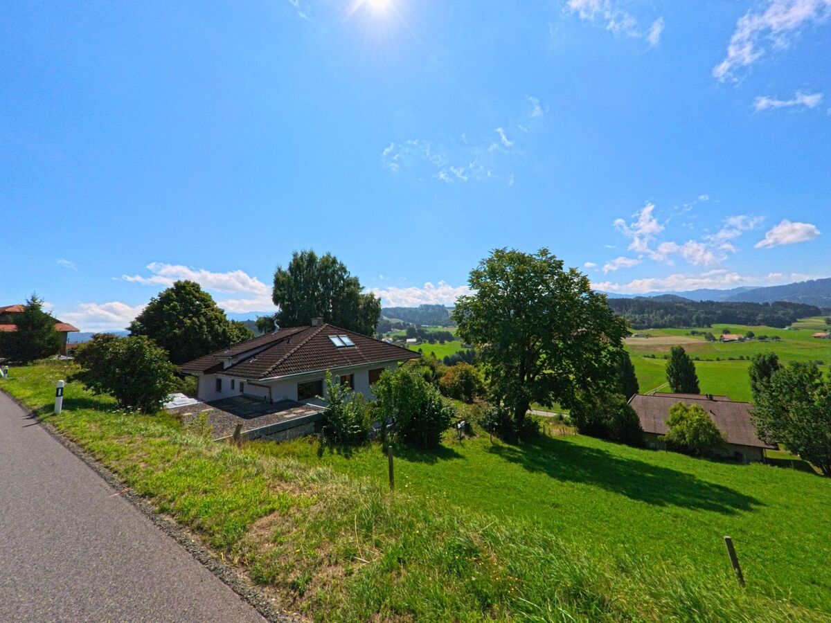 Von einer ansteigenden Strasse in Rechthalten (1718, Kanton Freiburg) bietet sich ein weiter Blick ueber Wohnhaeuser, gruene Felder und bewaldete Huegel.
