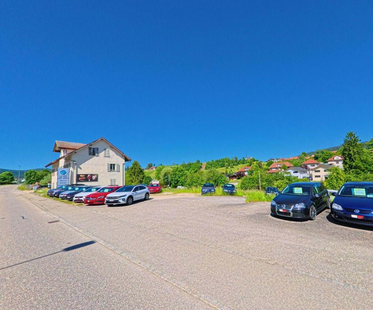 In Reconvilier (2732, Kanton Bern) befindet sich ein Autohaus mit grossem Aussenareal für Gebrauchtwagen, umgeben von Hügeln und Wohnhäusern.