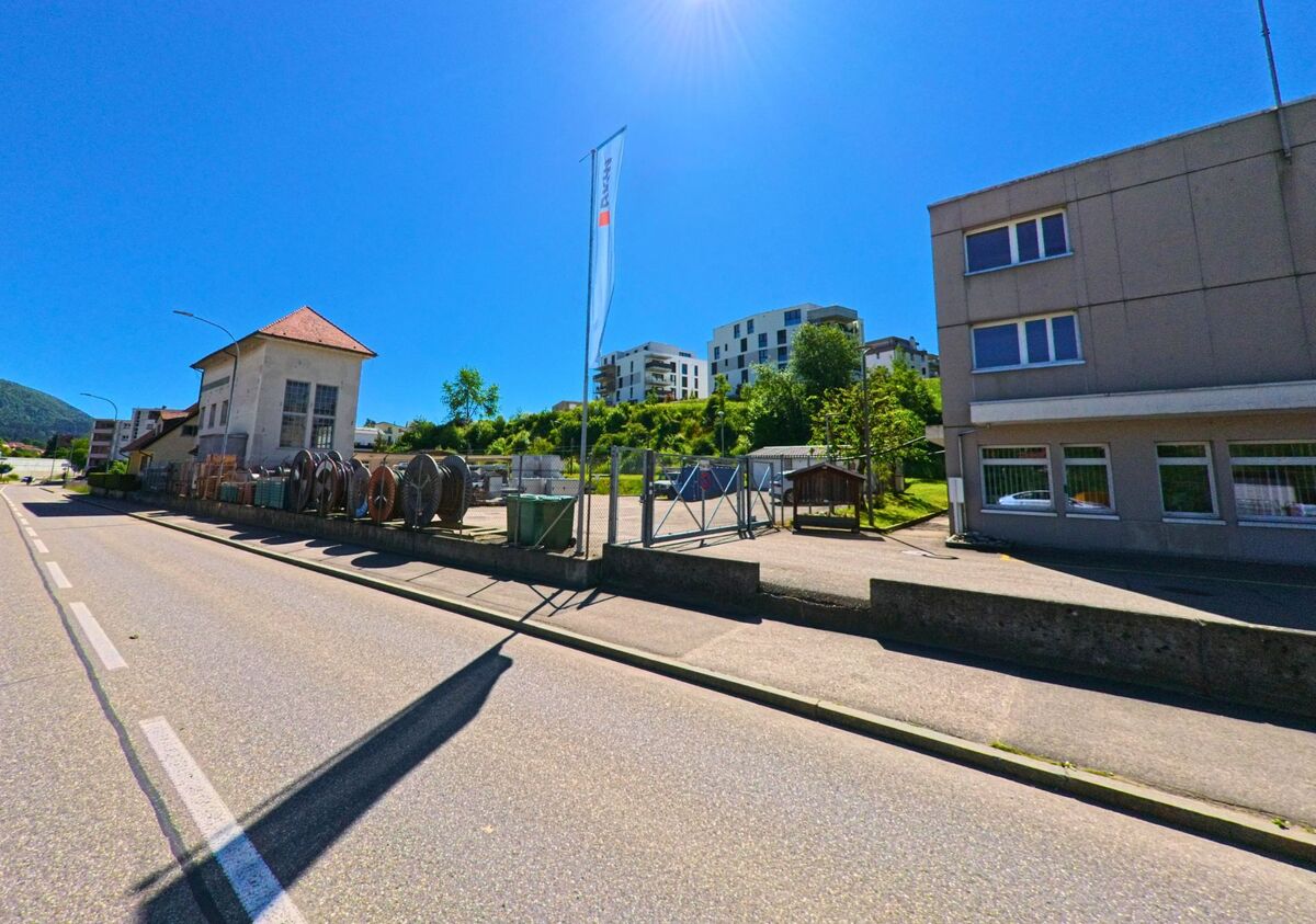 In Reconvilier (2732, Kanton Bern) befindet sich ein Industrieareal mit Kabelrollen und Werkstattgebäuden, dahinter ragen moderne Wohnhäuser über die Anhöhe.