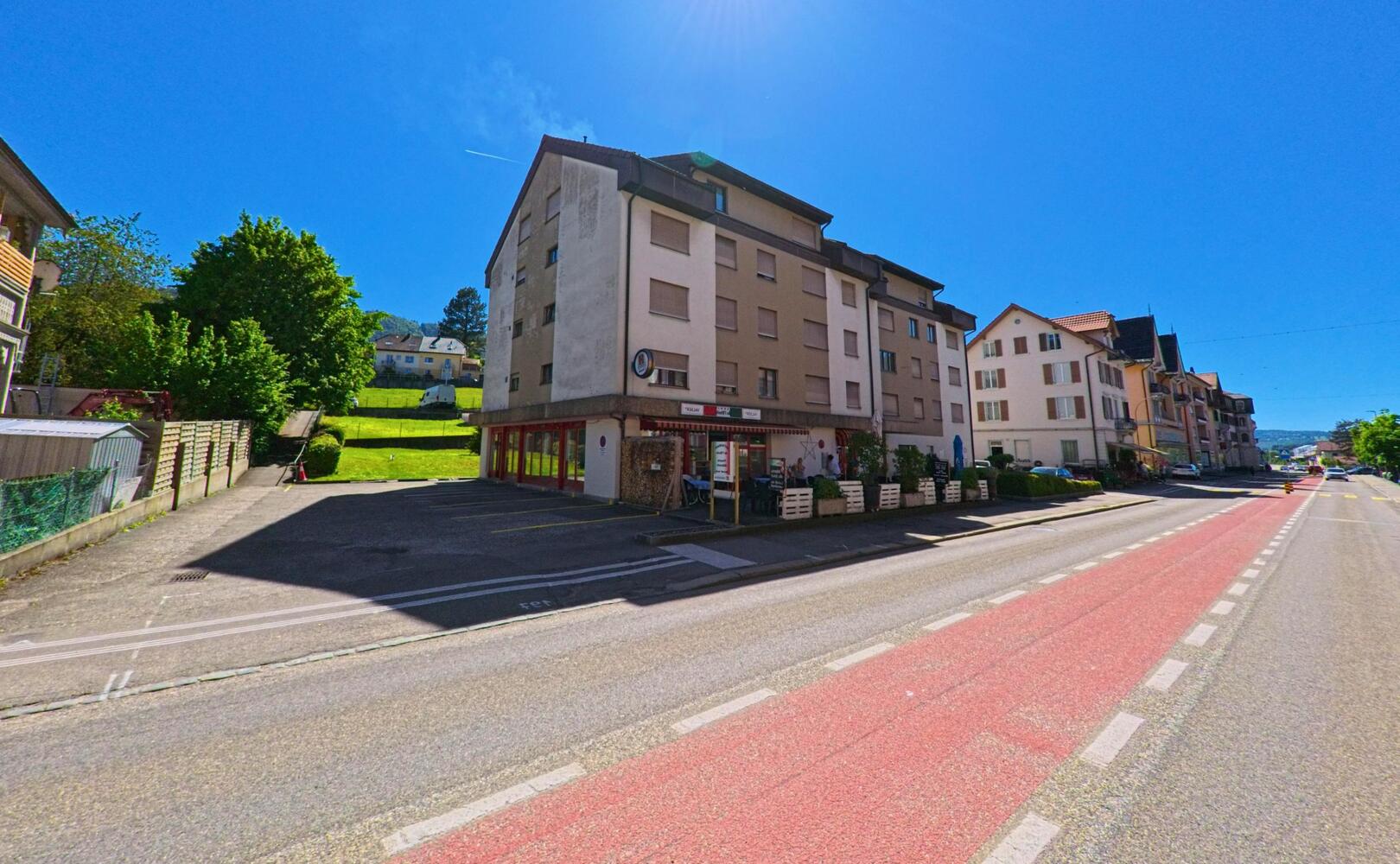 In Reconvilier (2732, Kanton Bern) liegt ein Wohn- und Geschäftshaus mit Laden im Erdgeschoss an einer Hauptstrasse mit markierter Radspur.