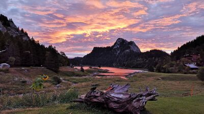 Beim Refuge La Vouivre in Miex (1896, Kanton Wallis) spiegelt sich der Abendhimmel in kräftigen Farben über einem See, umrahmt von Bergen und Wäldern.