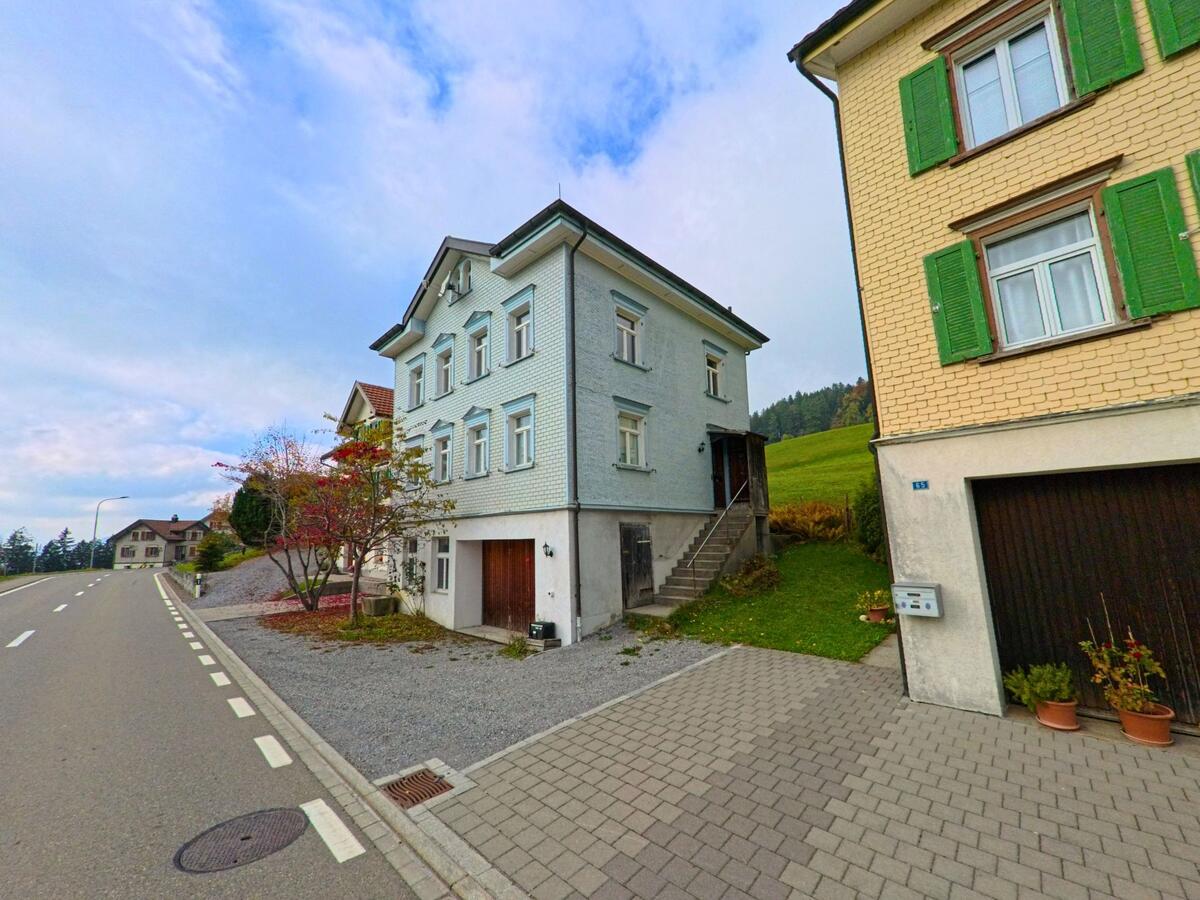 Vor Wohnhäusern mit Vorgärten verläuft eine gepflasterte Zufahrt in Rehetobel (9038, Kanton Appenzell Ausserrhoden).