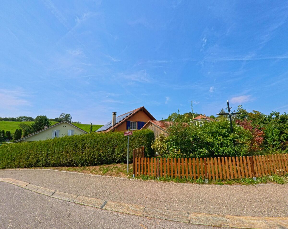 Ein Wohnhaus mit Solarpanelen auf dem Dach steht in Remaufens (1617, Kanton Freiburg) hinter einer Hecke und einem Holzlattenzaun an einer ruhigen Strasse.
