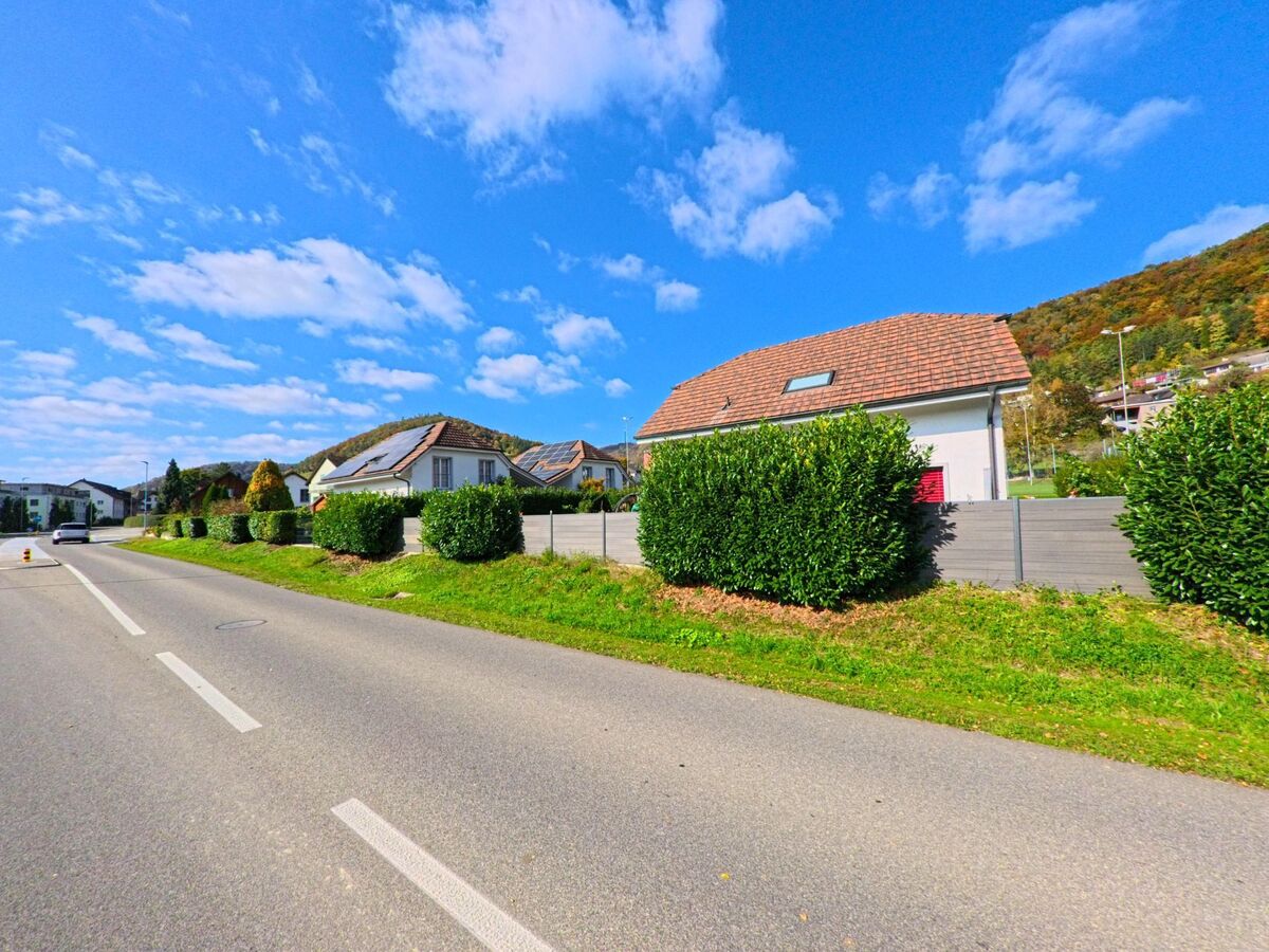 Moderne Einfamilienhäuser mit Solaranlagen stehen entlang einer breiten Strasse in Remigen (5236, Kanton Aargau) unter blauem Himmel.