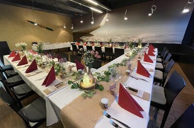 Im Restaurant Belpmoos in Belp (3123, Kanton Bern) sind festlich gedeckte Tische mit roten Servietten und Blumenschmuck fuer eine Feier vorbereitet.