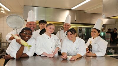 In der Küche des Restaurant de Courtemelon in Courtételle (2852, Kanton Jura) posiert das Küchenteam fröhlich in Kochkleidung mit Küchenutensilien.