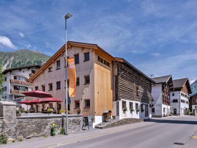 Das Restaurant Miraina in Klosters-Serneus (7250, Kanton Graubuenden) befindet sich in einem modernisierten Holzbau mit Terrasse und roten Sonnenschirmen.