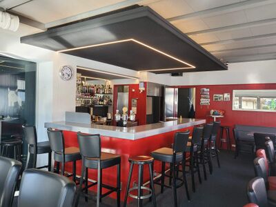 Im Restaurant Oxä in Oberuzwil (9242, Kanton St. Gallen) befindet sich eine moderne Bar mit roten Elementen, schwarzen Barstuehlen und gut sortiertem Getraenkeregal.